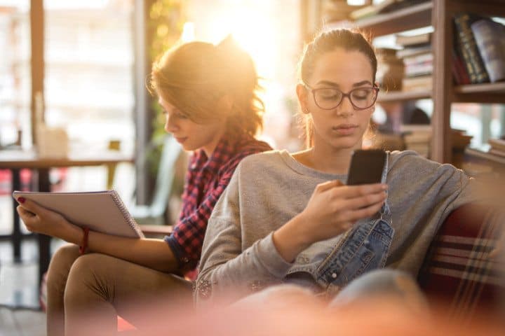 Young woman relaxing with her friend while using cell phone
