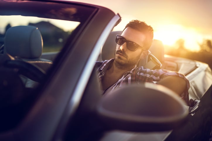 Young man driving a convertible car at sunset.