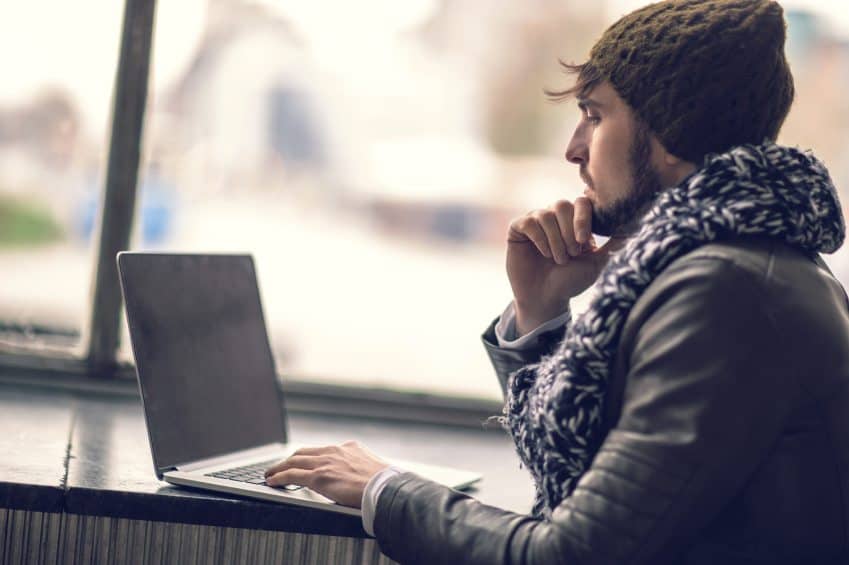 Profile view of pensive hipster man using laptop.