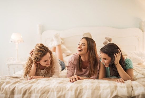 three female friends laughing in bed