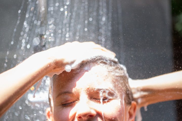 Woman washing hair in outdoor shower.