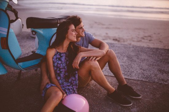 couple leaning on scooter on beach
