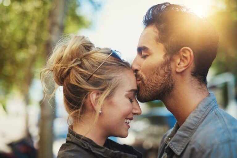man kissing woman's head sun