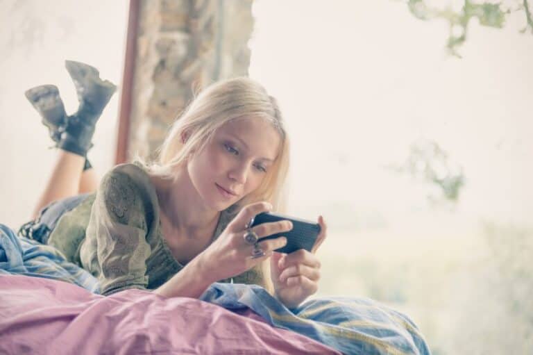 Blonde laid on bed with smartphone