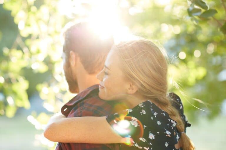 Young adult couple outside trees hugging