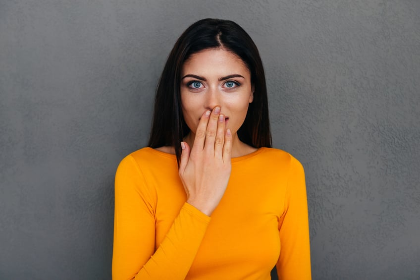Surprised young woman covering mouth with her hand.