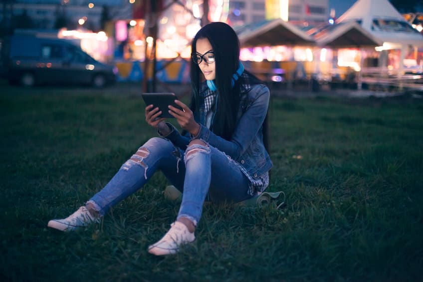 Girl sitting on a grass field in front of illuminated cityscape