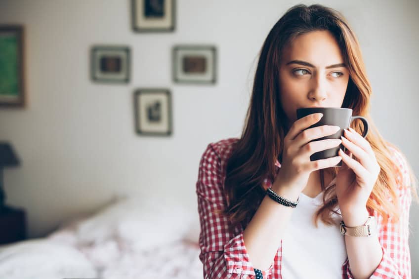 Young woman standing at bedroom and drinking coffee