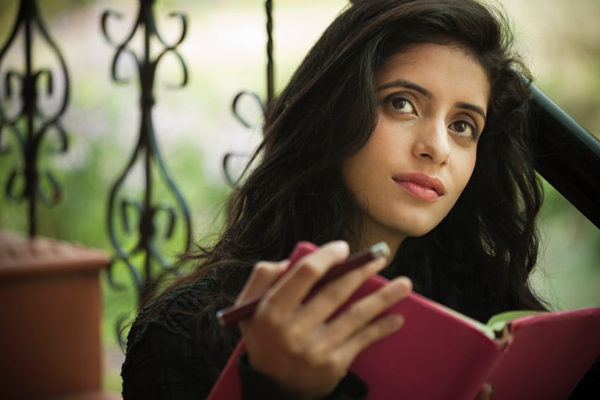 Happy late teen girl student thinking while holding a book