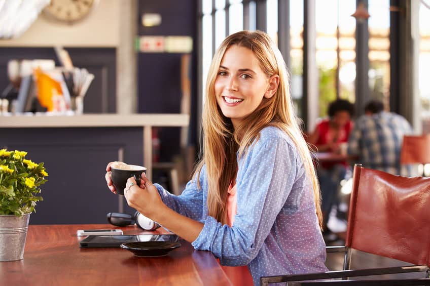 Young woman drinking coffee at a coffee shop, smiling to camera