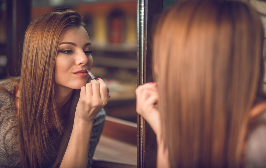 Young woman applying lipstick in the mirror.