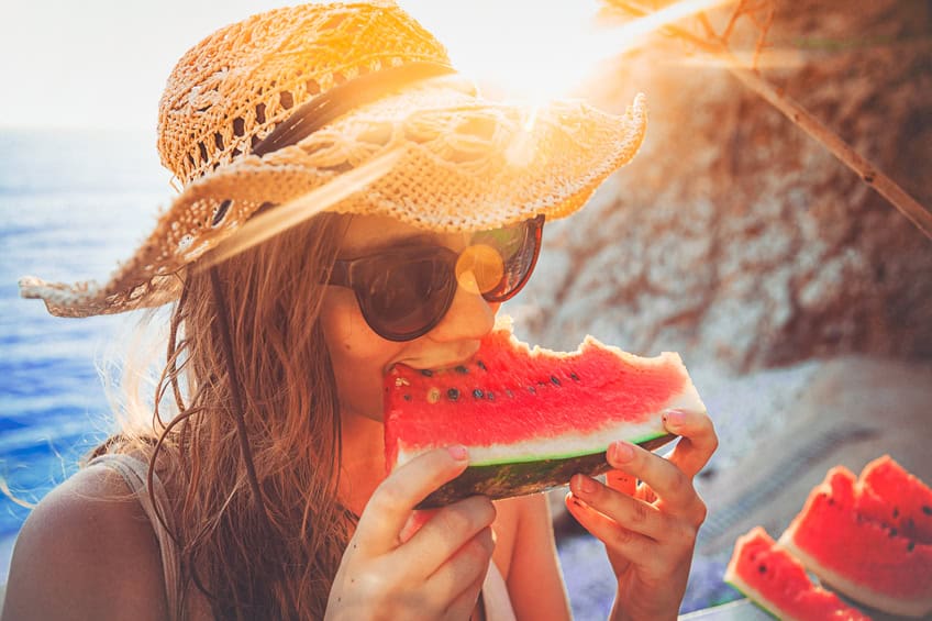Woman on the beach eating watermelon.