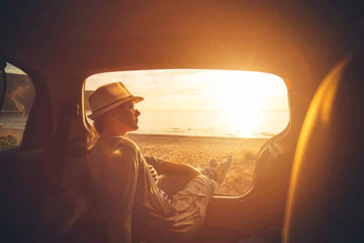 Young woman sitting in the trunk of a car on a beach in sunset
