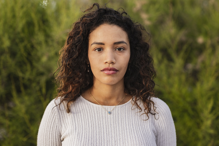 serious millennial woman outdoors green background