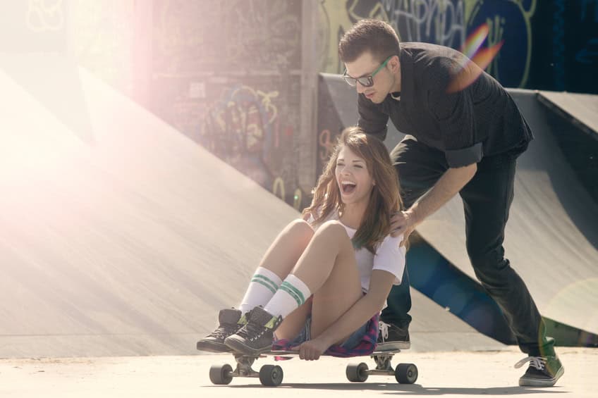 man pushing woman skateboard sunshine
