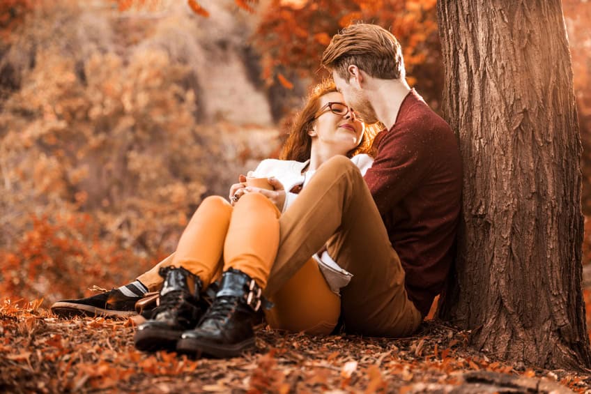 Happy red-haired couple sitting embraced in the park and enjoying in autumn day.