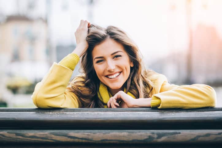 Beautiful smiling woman sitting on a bench enjoying the sunlight outdoors in the city, with copy space