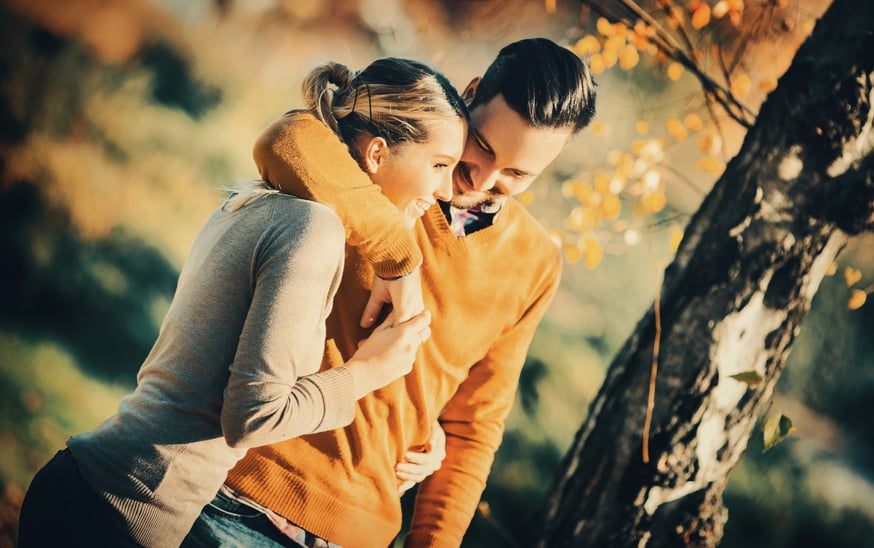 Closeup of happy late 20's couple taking a walk in a park on a warm september day. Enjoying together and walking embraced. Bothe wearing light sweaters. Tilt shot, toned.
