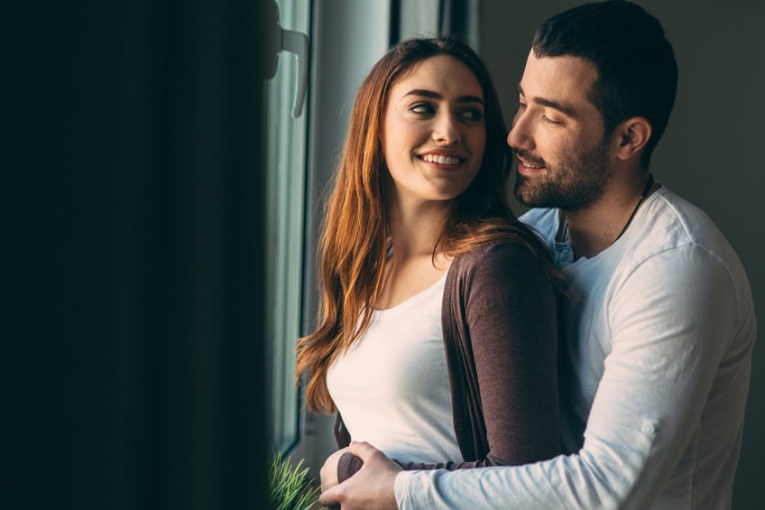 Husband and wife hugging next to the window.