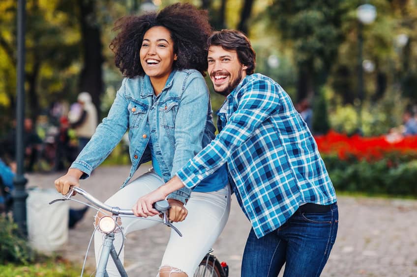 Young man helping his girlfriend to ride a bike, outdoors in the park.