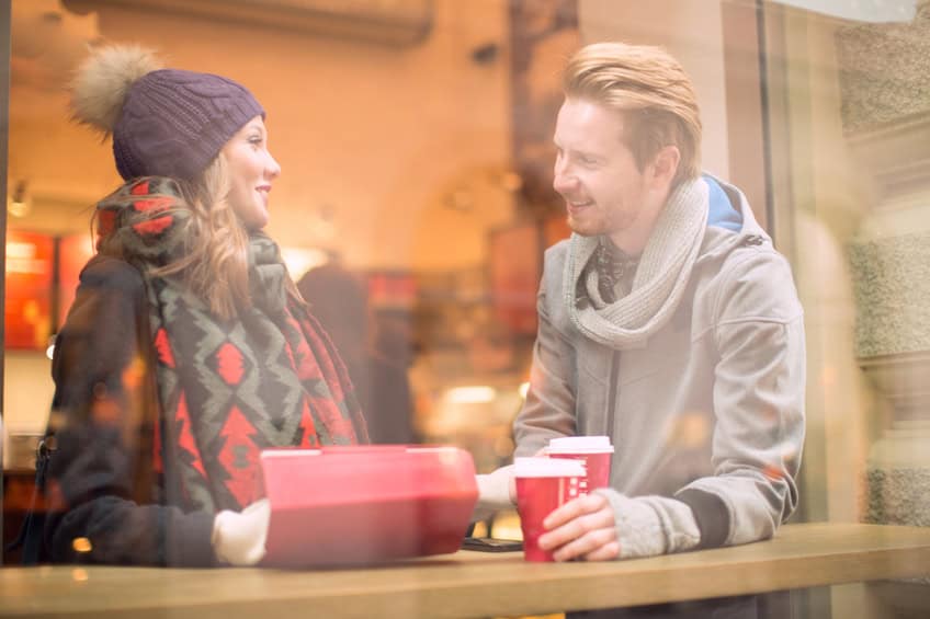 Friends or couple drinking coffee and using digital tablet at cafe in city centre. Vienna, Austria. Wearing warm clothes. Photographed from outside through the window.