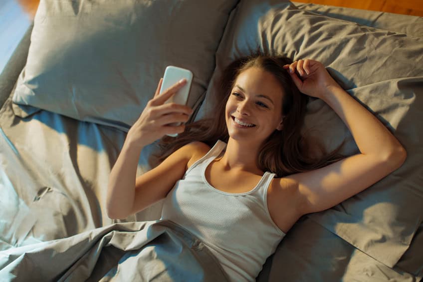 Close up of a young woman using smart phone while lying in bed