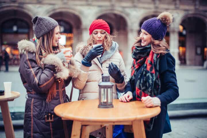 Friends drinking hot wine outdoors at winter city street, christmas market. Wearing warm clothes. Vienna, Austria. Smiling and talking.