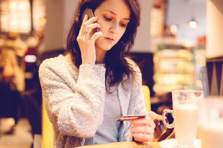 Young woman in a cafe phoning the bank for credit card support.