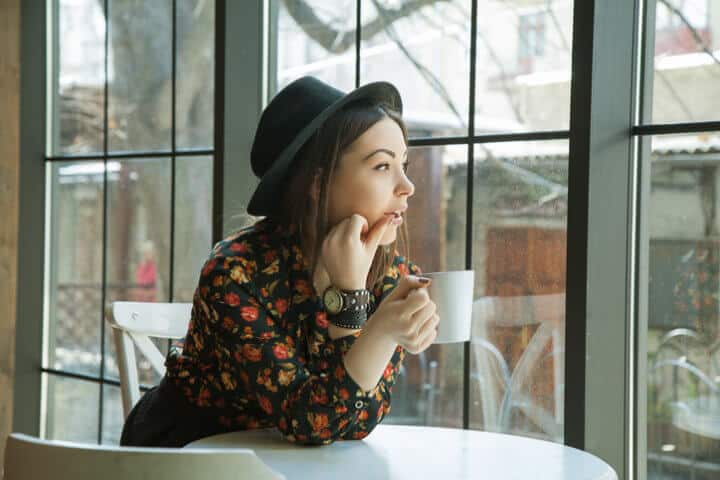 beautiful woman in hat drinking coffee in the morning sitting by the window. view from inside.