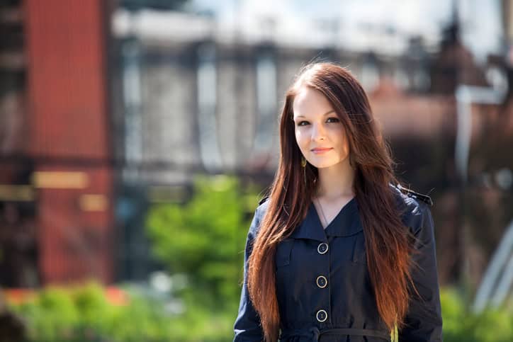 Portrait of young woman in front of industry background. She is serious and has wearing a summer blue cloak.