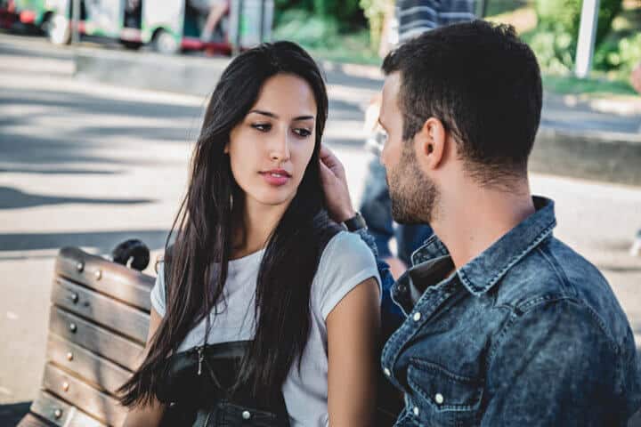 Couple sitting on a park bench looking at each other on a suuny day