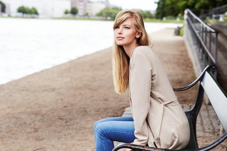 Thoughtful young woman on bench by river