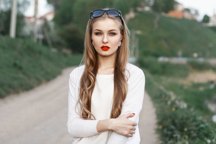 Beautiful portrait of a young woman with red lips and sunglasses. On the background of the road and the green fields. Spring time.