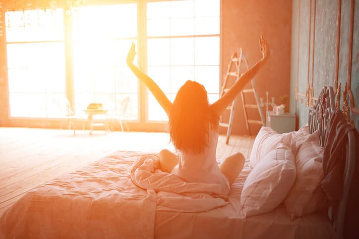 young woman stretch bed morning sun