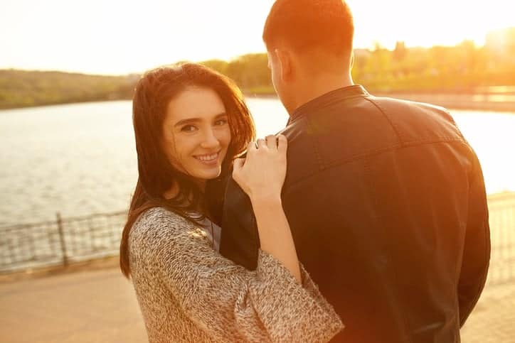Happy couple at sunset. Young woman leaning on her boyfriend back. Smiling girl looking at camera on a sunny autumn day with copy space. Lens flare effect