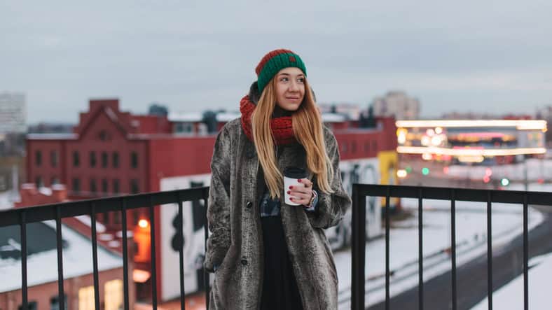 Attractive girl with a cup of coffee stands on a background of a beautiful European city