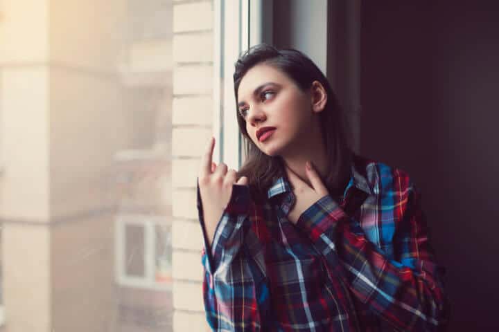 Beautiful young woman sitting casually, leaning and looking through the window