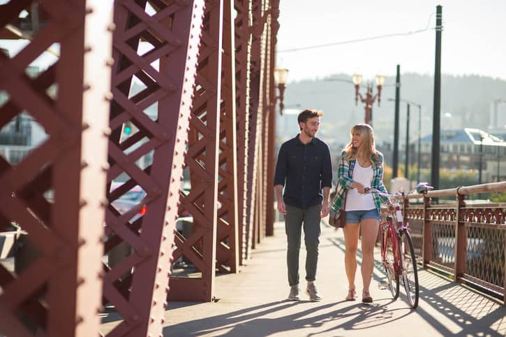 Attractive young adult couple walking and riding a bike across a city bridge