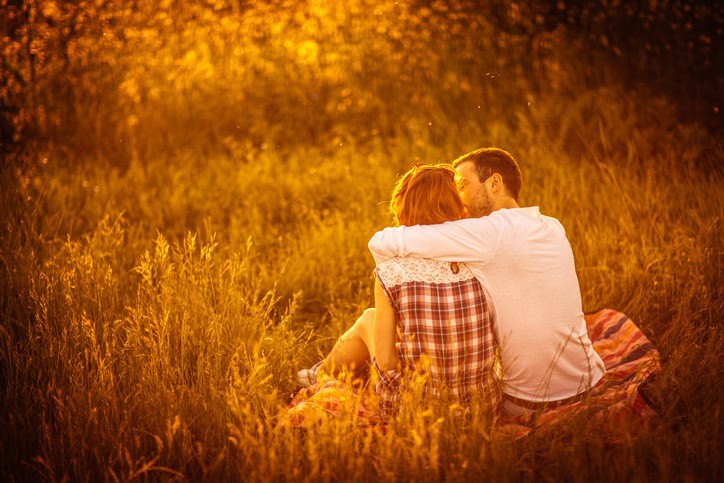 Photo of young couple sitting and hugging in a meadow