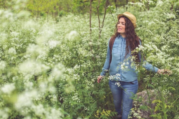 Beautiful caucasian girl with a backpack on her shoulders exploring nature full of blooming flowers in spring.