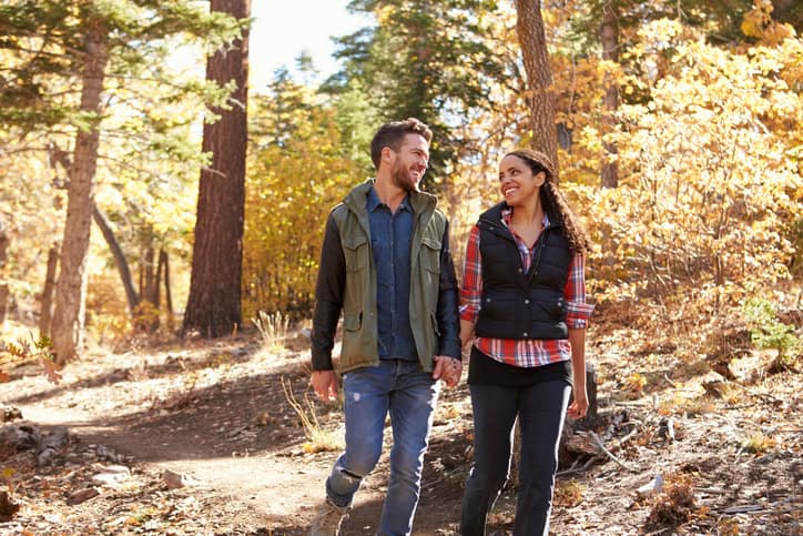 Couple hiking in a forest hold hands and look at each other