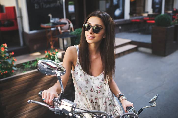 young attractive girl with a beautiful smile wearing a light dress and vintage old scooter near a cafe on summer day