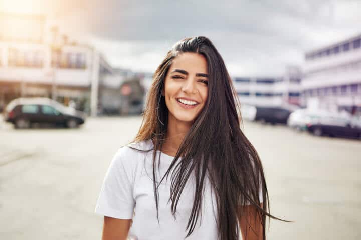 Smiling young woman in long brown hair and white short sleeve shirt walking in the middle of street