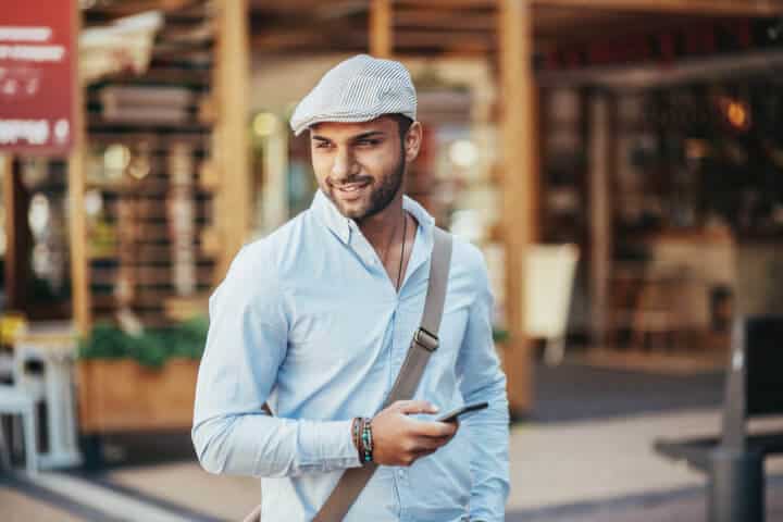 Young man holding a smart phone and walking on the street, looking away.