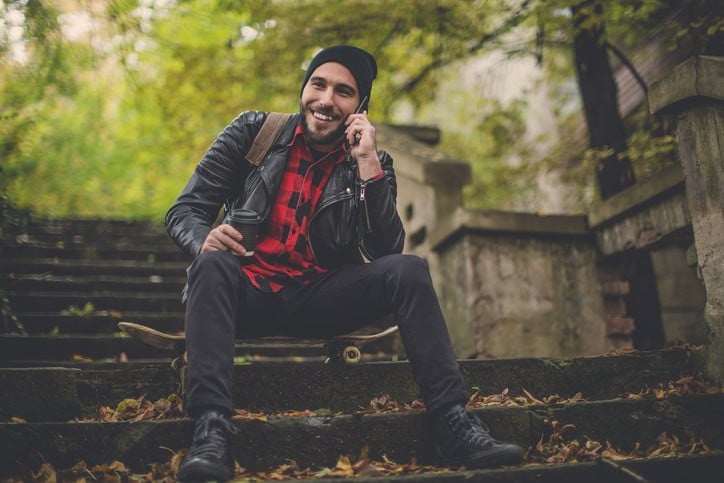 Hipster talking on the phone while sitting on a skateboard on the stairs in the park.