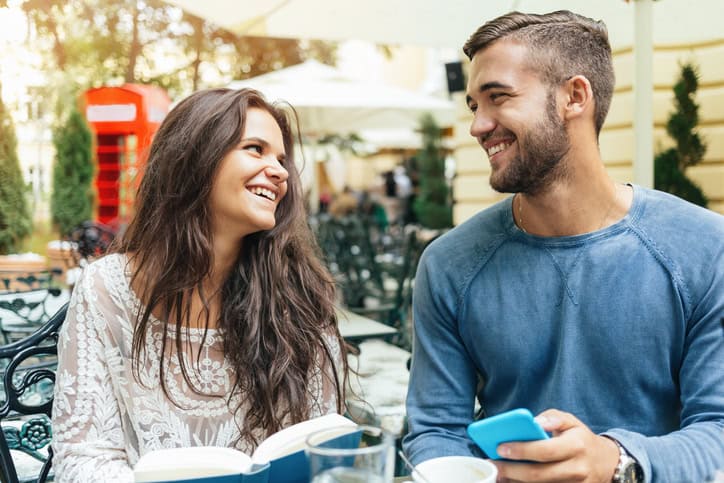 Young couple having fun while sitting in a coffee shop. The girl is reading a book and the boy is playing with his cell phone.