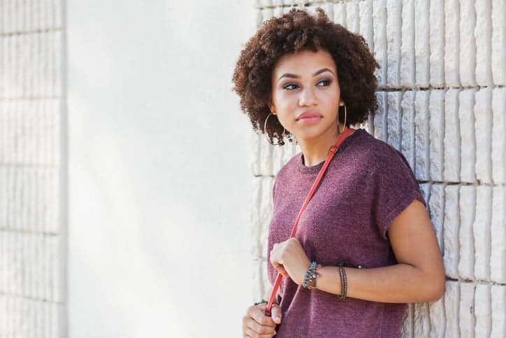 Young African American woman (19 years), standing outdoors, leaning against building.