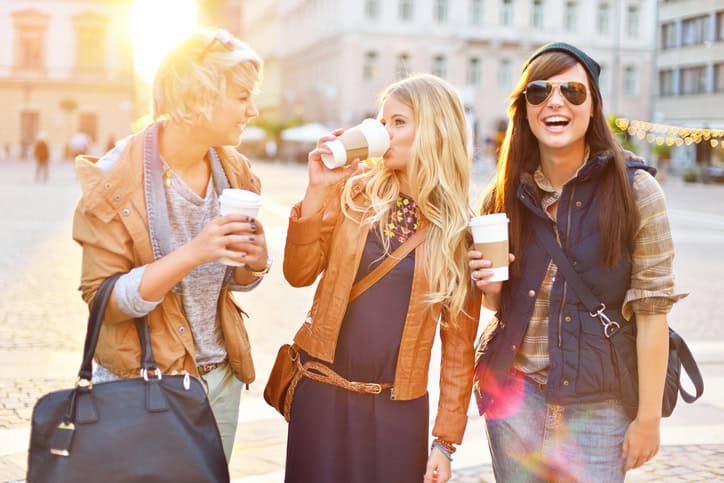 Young friends together walking in the city, talking and drinking coffee from paper cup.