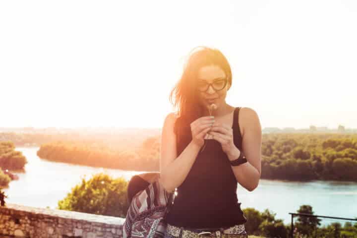 Beautiful woman enjoying summer holding flower with sun flare.