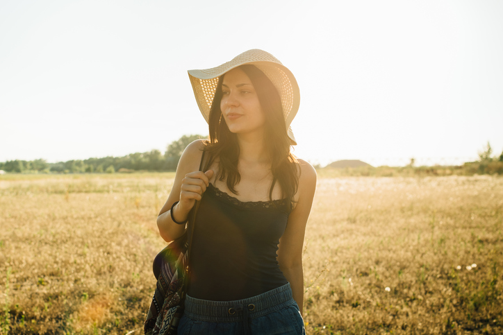 Fashionable girl walking in nature wearing hat, enjoying summer